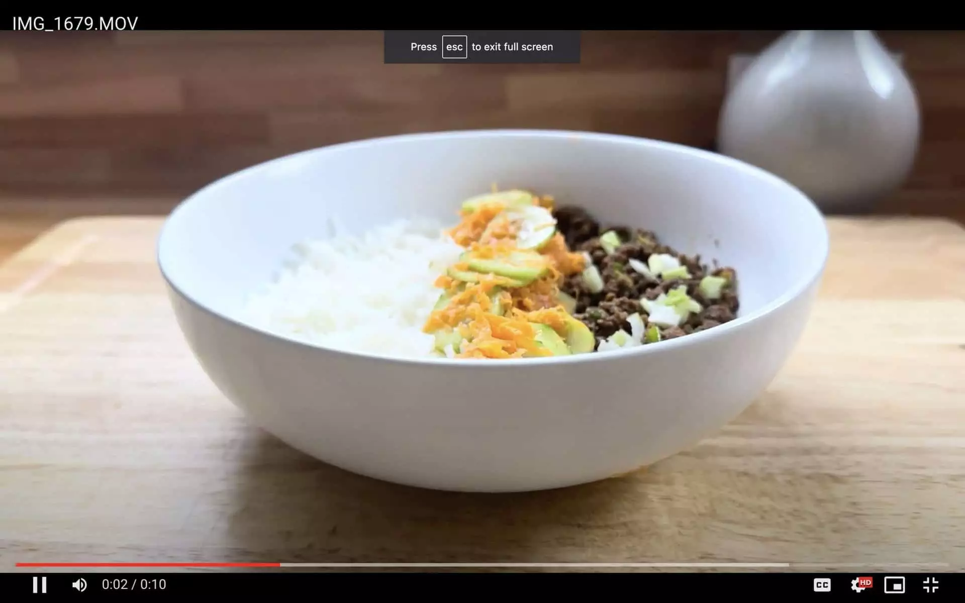 Bowl of white rice, avocado, grated carrots, and ground beef on a wooden table.